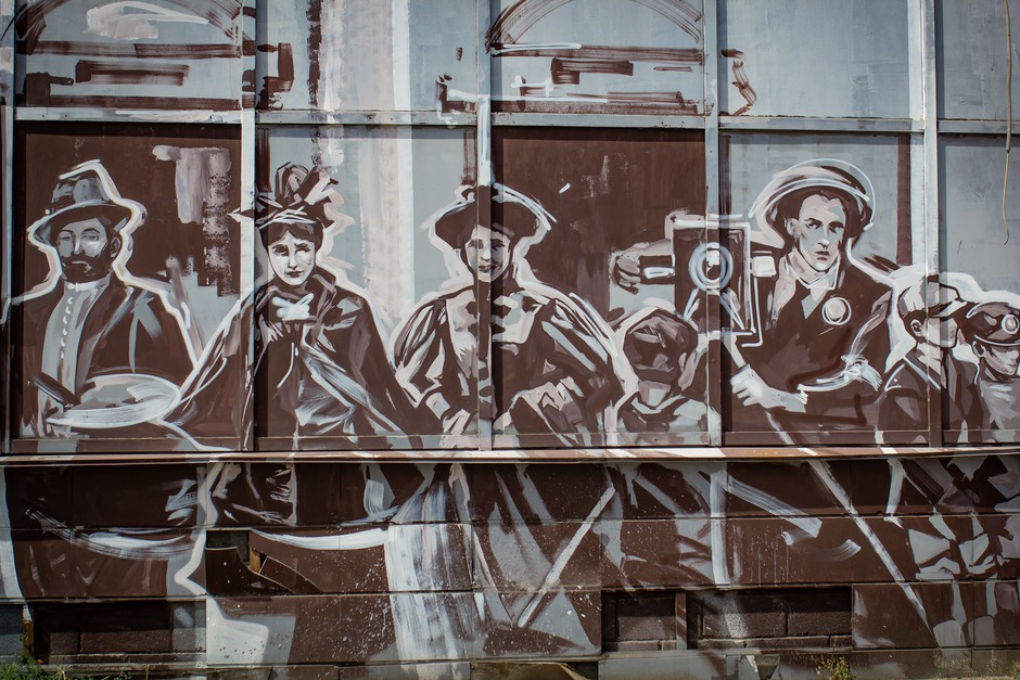 На фоне фасада «Гиганта» мы видим прохожих, которые куда-то спешат, их след размывается в пространстве