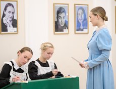 За старинной партой, используя перьевые ручки, под руководством старшеклассниц в образах гимназисток и учительниц начала XX века, гости писали поздравительные открытки.